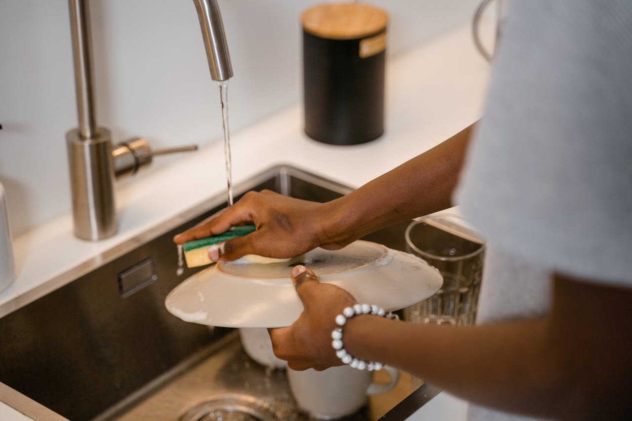 Person cleaning dishes in a modern kitchen sink using running water.